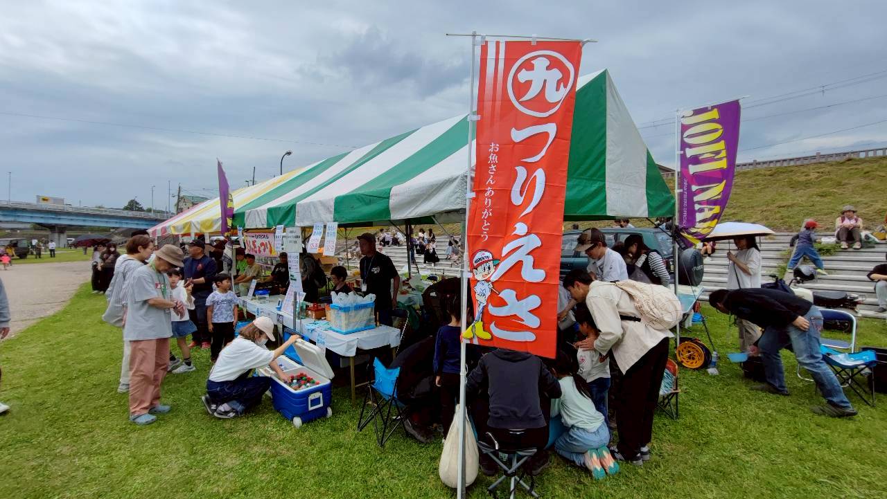 吉野川の河川敷の金魚釣り体験のテントに親子が集まる様子