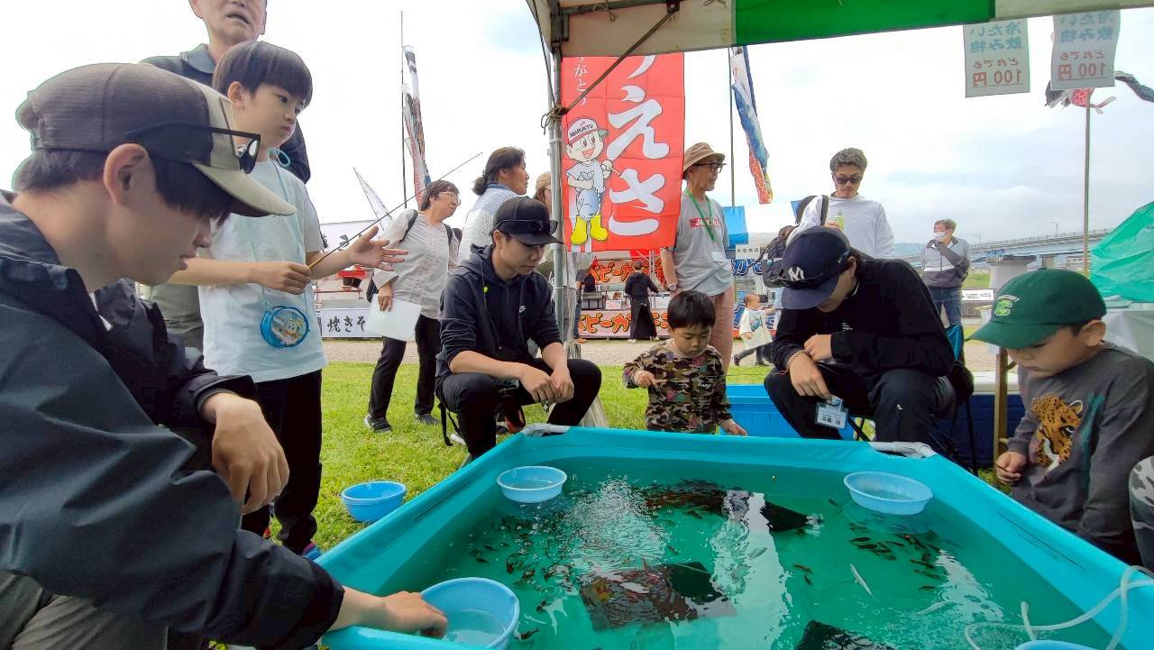 小さな釣り竿を持つ子どもたちの金魚釣りを、スタッフがそばで支える様子